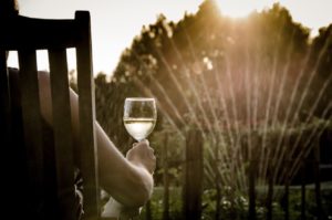 Woman enjoying a glass of wine as sprinklers turn on in her yard.